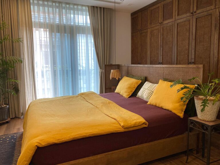 Phòng ngủ nhiệt đới với chăn ga gối linen vàng mù tạt và mây tre